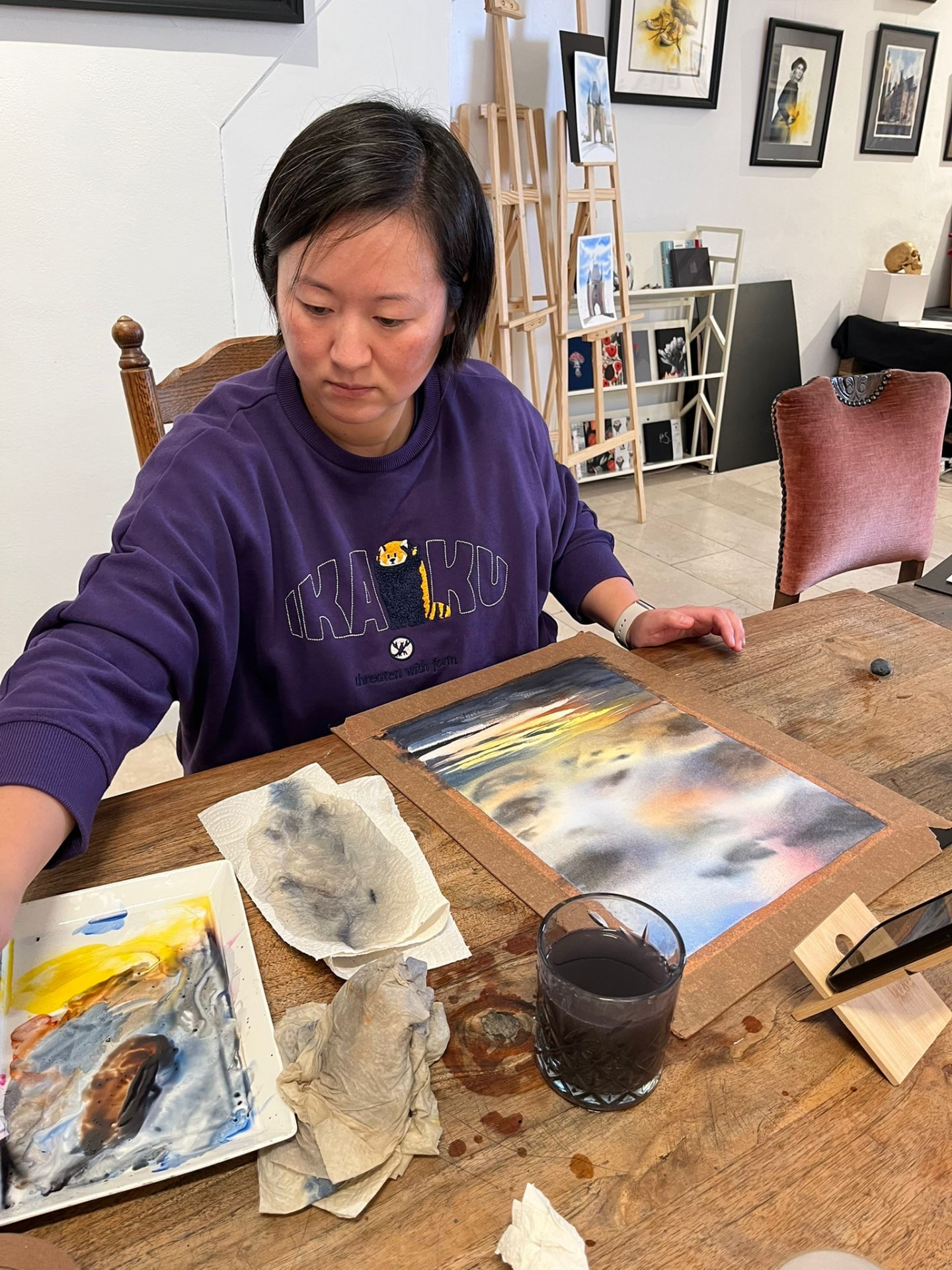 Amy seated at a wooden table in her studio, working on a watercolour landscape